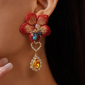 Détail de boucle d'oreille fleur rouge brodée avec cadre cœur doré et gemme goutte jaune