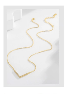 Detailed view of gold V-shaped pendant necklace with cubic zirconia on stone texture