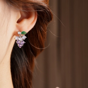 Close-up of purple grape-shaped drop earrings with green leaves on a female model
