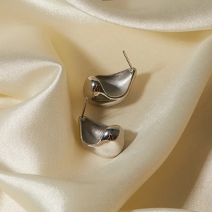 Macro detail of silver irregular curved drop earrings on a soft cream silk background
