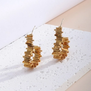 Elegante goldene geometrische Stapelwürfel-Ohrringe auf weißem Stein Hintergrund präsentiert