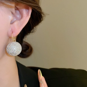 Detailed view of shimmering pave crystal ball earrings with elegant gold hooks on model