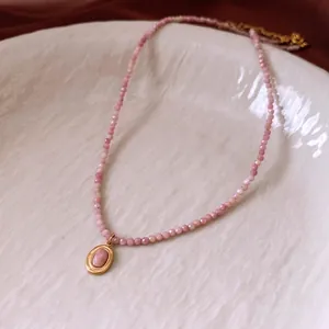 Pink beaded necklace with gold oval rhodochrosite pendant on textured ceramic tray
