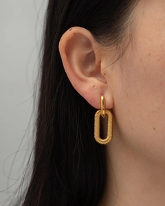 Golden titanium steel oval earrings with ribbed texture worn by a model in profile