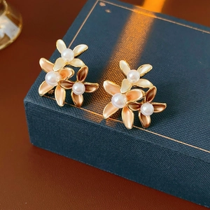 Macro view of gold-plated flower earrings with pearls on a textured navy jewelry box