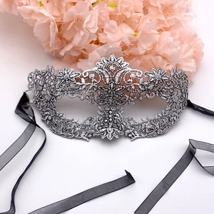 Close-up of silver lace masquerade mask with black ribbons on a white surface