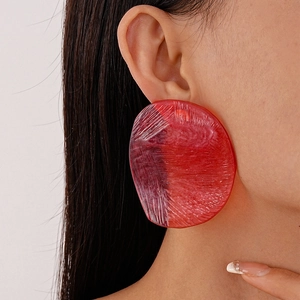 Close-up of a model wearing large red resin round earrings with textured brush strokes
