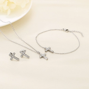 Detailed view of silver cross jewelry set with necklace bracelet and earrings on linen