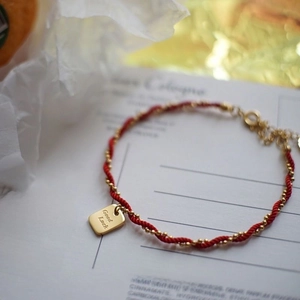 Red braided cord bracelet with gold beads and Good Luck engraved square pendant