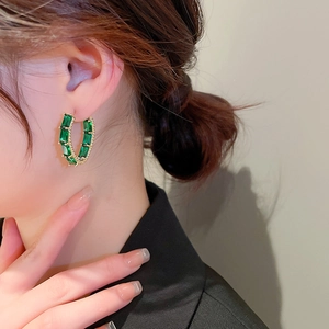 Close-up of a gold-tone C-shaped earring with emerald green zircon on model ear