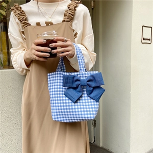 Detailed view of a plaid tote bag with a denim bow on a light textured wall background