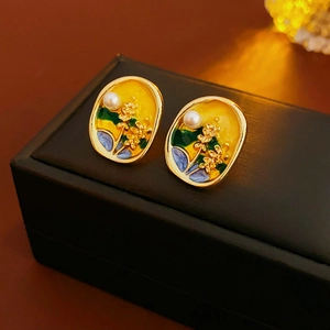 Detailed macro view of vintage oval gold earrings with floral enamel and a white pearl inlay