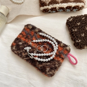 Close-up of plush plaid storage bag featuring jewelry, pearl necklace, and rings