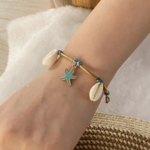 Gold ocean bracelet with turtle shell and blue starfish charms on a model's wrist