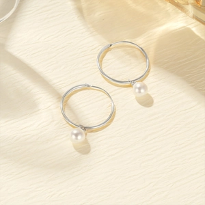 Close-up of S925 sterling silver hoop earrings with white pearl pendants on paper