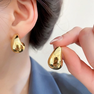 Detail view of golden irregular water drop earrings with a polished mirror finish on model