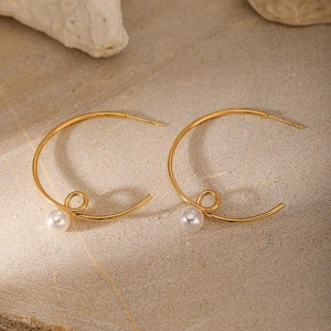 Detailed view of gold-plated twisted C-shaped earrings featuring a white pearl accent