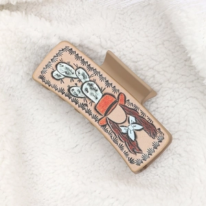 Western style beige hair claw clip featuring a cartoon cactus girl on a white plush rug