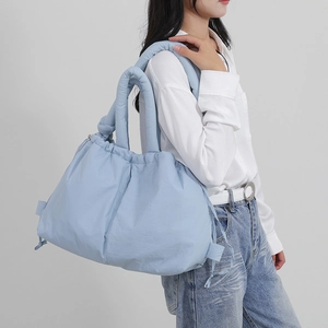 Light blue padded nylon drawstring tote bag worn by a model in casual outfit