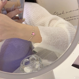 Dettaglio del bracciale di perle dorate con una gemma rosa a forma di cuore al polso
