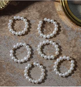 Macro shot of six elastic freshwater pearl rings with 14K gold filled beads on beige texture