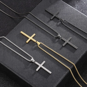 Three matte cross necklaces in black, gold, and silver on a textured gift box