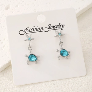 Blue turtle and starfish drop earrings with crystal accents on a white jewelry card