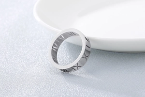 Close-up of titanium steel ring with hollow Roman numeral cutouts on grey background