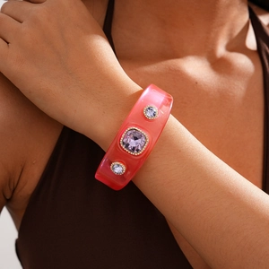 Close-up of wide orange resin bracelet with purple square crystals in gold settings