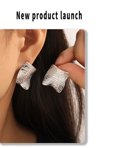 Macro detail of irregular square silver earrings with textured cross-grid finish