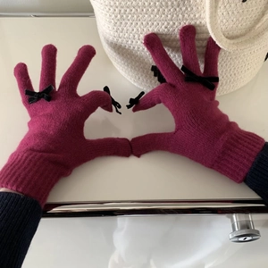 Close-up of pink knitted gloves with small black bow details showing heart gesture