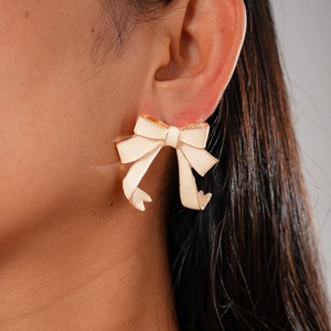 Close-up of elegant cream bow earrings featuring a vintage gold trim on a model's ear