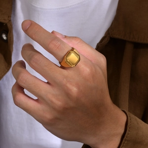Polished gold square signet ring for men worn on finger against a brown jacket background
