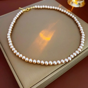 Close-up of elegant champagne pearl necklace with gold clasp in a beige jewelry box