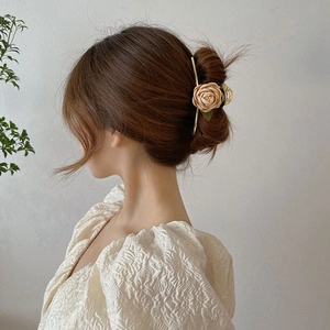 Detail of elegant gold metal hair claw clip with cream fabric rose on a bun hairstyle