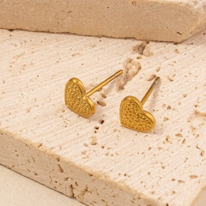 Macro shot of gold heart stud earrings with fine textured surface on beige stone