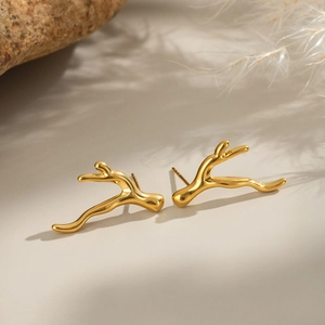 Boucles d'oreilles branche dorée minimalistes sur surface beige et éléments naturels