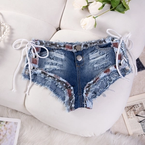 Dettaglio di shorts in denim a vita bassa con lacci laterali e bordo con motivo a stelle