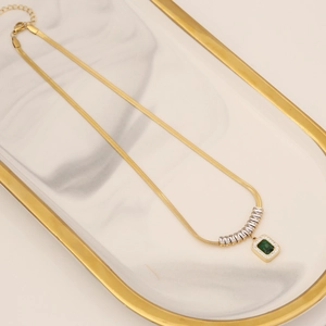 Golden snake chain necklace with square emerald zircon pendant on marble tray