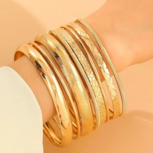 Detail of stacked gold alloy bracelets with diverse textures including snake and spiral patterns