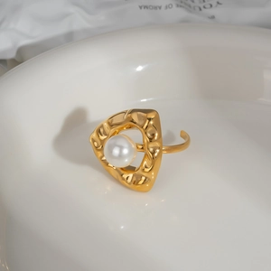 Détail d'une bague dorée triangle irrégulier avec perle blanche sur plateau céramique
