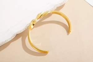 Detailed view of a gold-plated twisted knot bangle with polished metallic finish