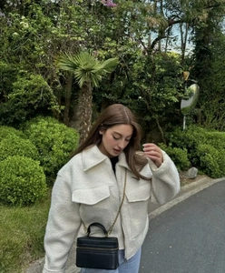 Detail of off-white sherpa jacket with lapel collar, zip pockets and black leather bag