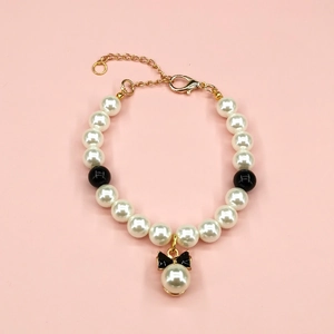 Detail of beaded pet necklace with white faux pearls and black bow pendant with gold clasp
