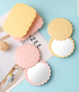 Flat lay of pink and yellow cookie-shaped folding makeup mirrors with combs on blue background