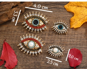 Detailed sizes of retro evil eye brooches with rhinestones and pearls on wood background