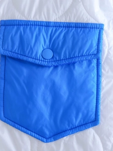 Dettaglio della giacca trapuntata bianca con tasca applicata blu e bottone a pressione