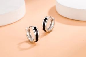 Close-up of silver hoop earrings with black enamel inlay on smooth beige background