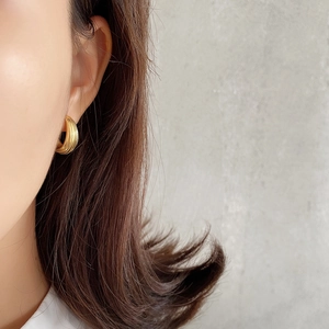 Close-up of a model wearing textured gold-toned C-shaped hoop earrings with a ridged finish