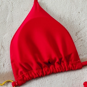 Close-up of red triangle bikini top with pleated details and gold ring metal accents